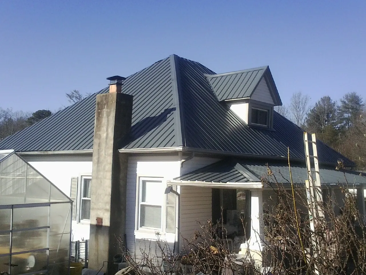 Dark blue standing seam metal roof on a white farmhouse with dormer — Slate & Tile Roof Repair by Roofing Brothers in Pfeifer