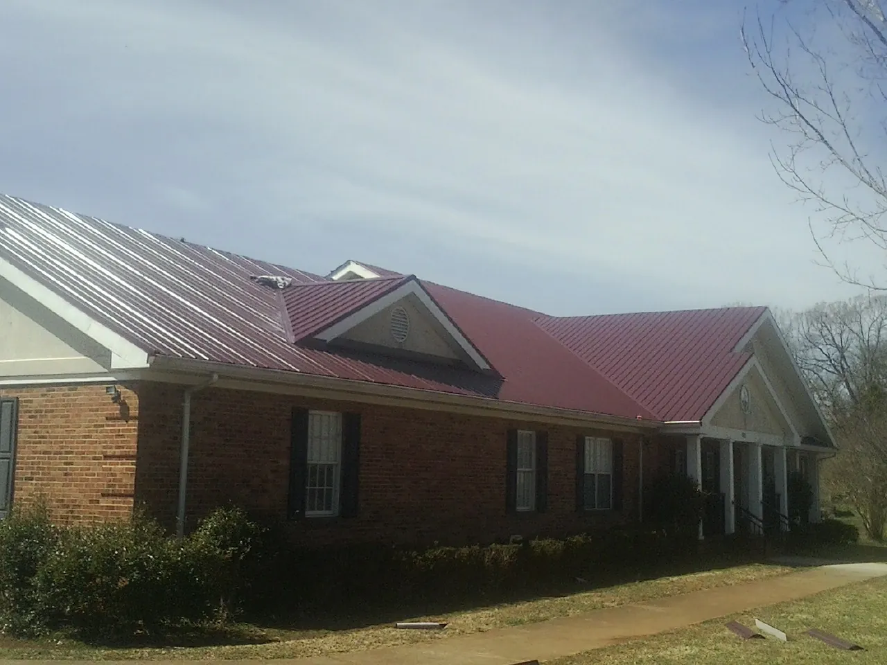 Red metal roof with gabled entries on a long brick building, from a Hail Damage Roof Repair job in Pfeifer