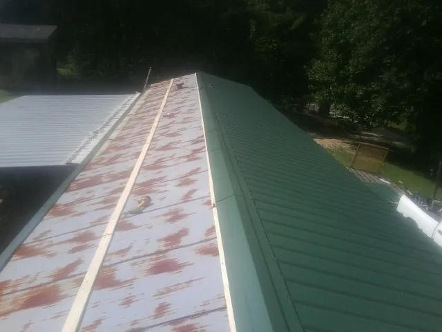 Old rusted panels beside newly installed green metal roofing — Wind Damage Roof Repair by Roofing Brothers in Pfeifer