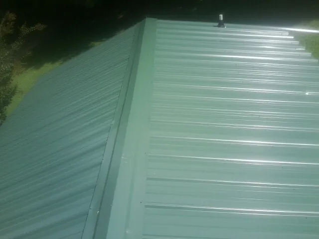 New green metal panels meeting at the ridge of a roof — Flat Roof Repair work by our crew in Pfeifer
