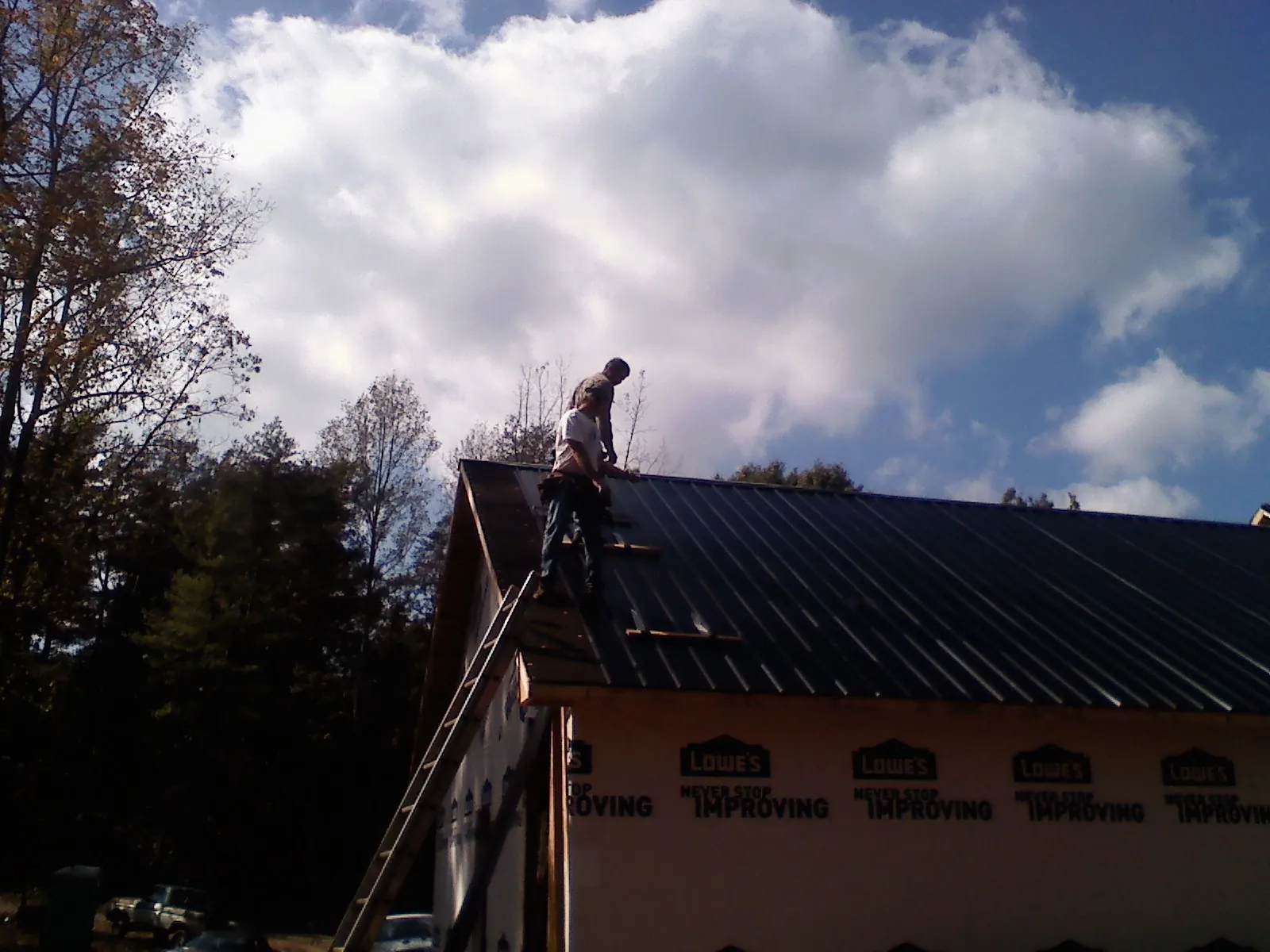 Roofer fastening dark metal panels high against a cloudy sky, from a Roof Inspection job in Pfeifer