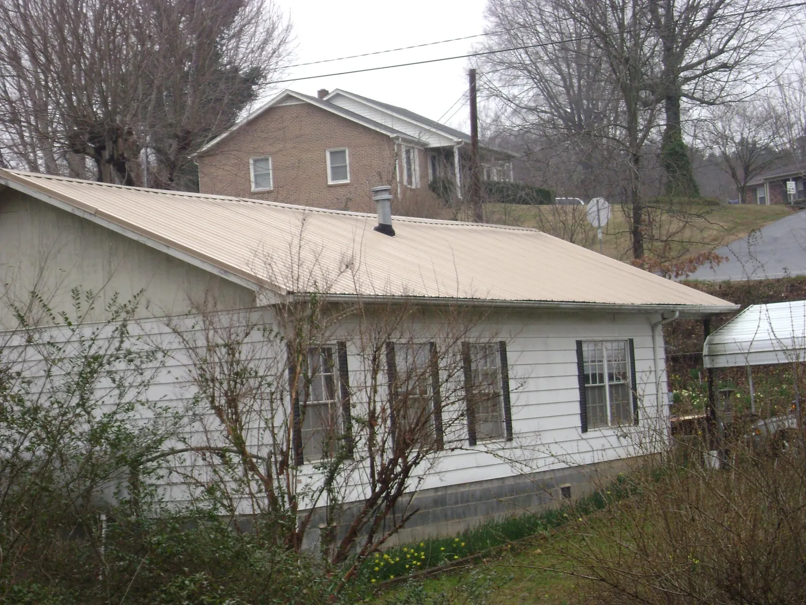 Tan metal roof on a white sided house set into a hillside — Commercial Roofing by Roofing Brothers in Pfeifer