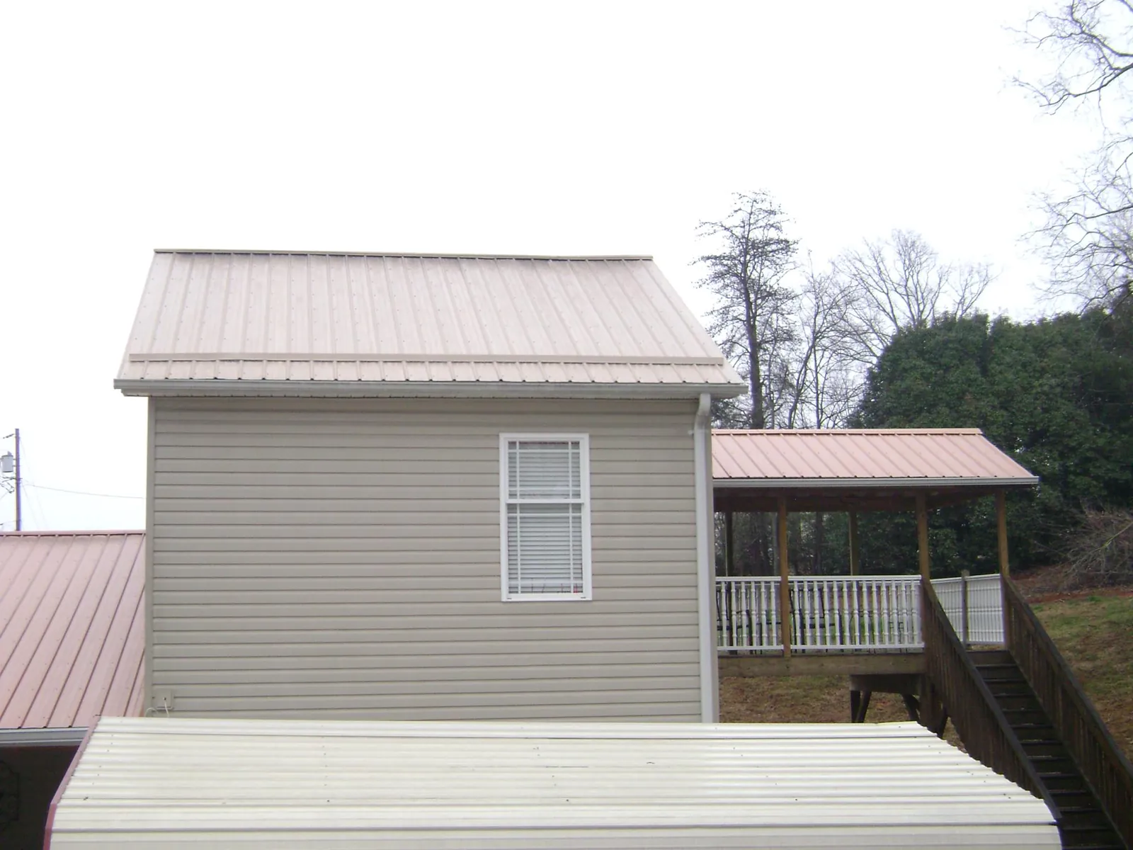 Tan metal roofs on a two story addition and attached porch, from a Roof Replacement job in Pfeifer